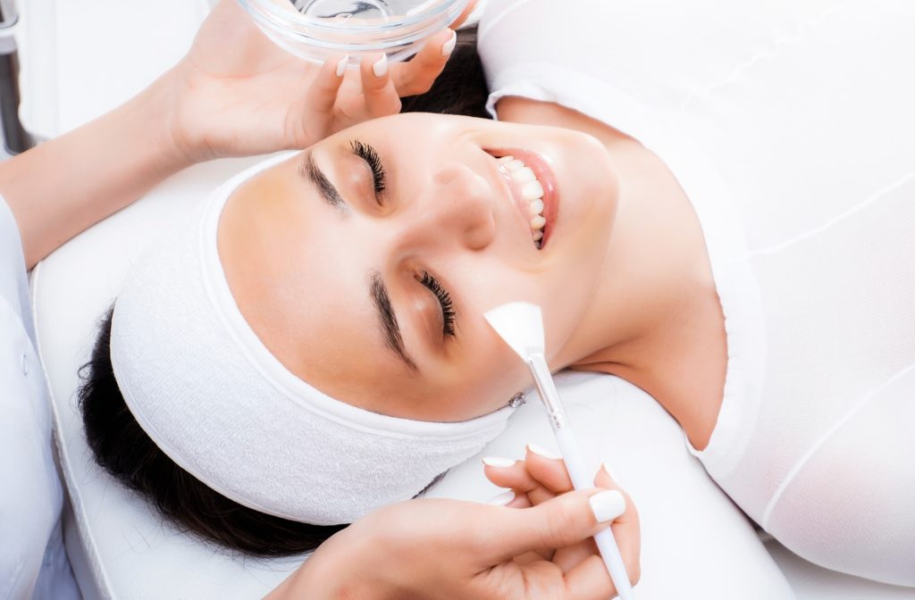 A woman laying down smiling, receiving a chemical peel to smooth and brighten her skin