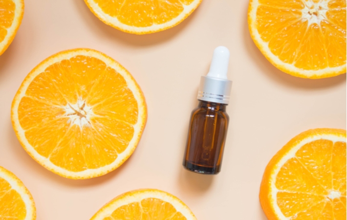 A bottle of vitamin c serum surrounded by sliced oranges