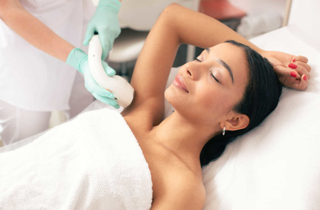 A young woman calmly laying down with her arm up, receiving laser hair removal on her armpit.