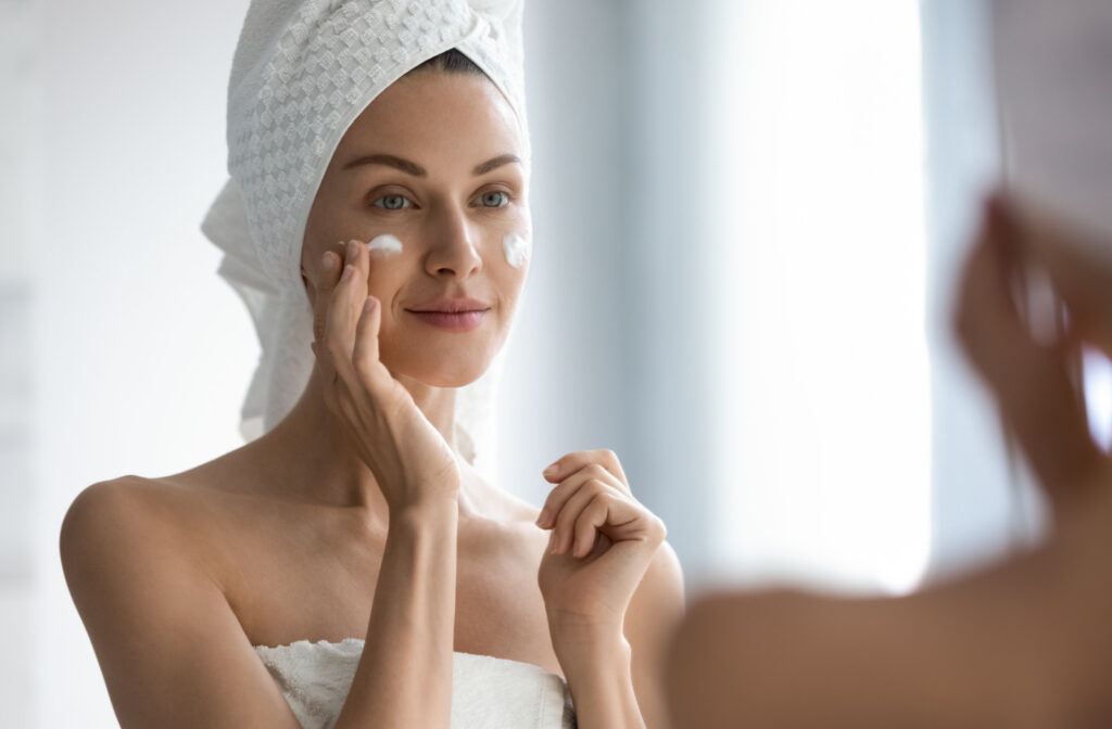 A woman looking in the mirror while moisturizing her face because her skin feels dry.