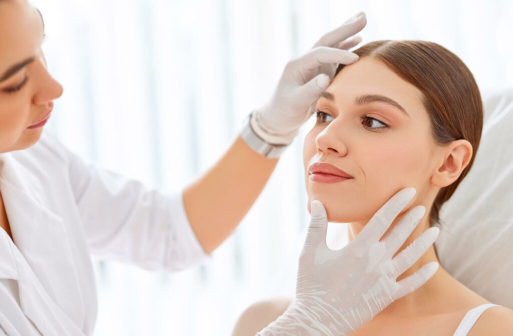 A female aesthetician analyzing a young woman's face in a clinic.