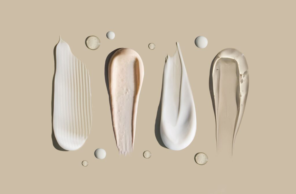 Swatches of different cosmetic creams and gels on a beige surface.