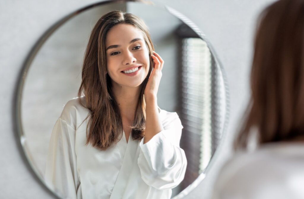 A woman looks into a mirror smiling because her skin tightening treatment is successful.