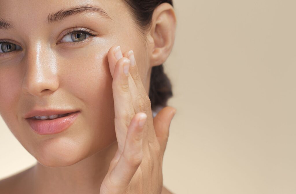 A close-up image of somebody touching their cheek and smiling, showing off the results from their professional facial.