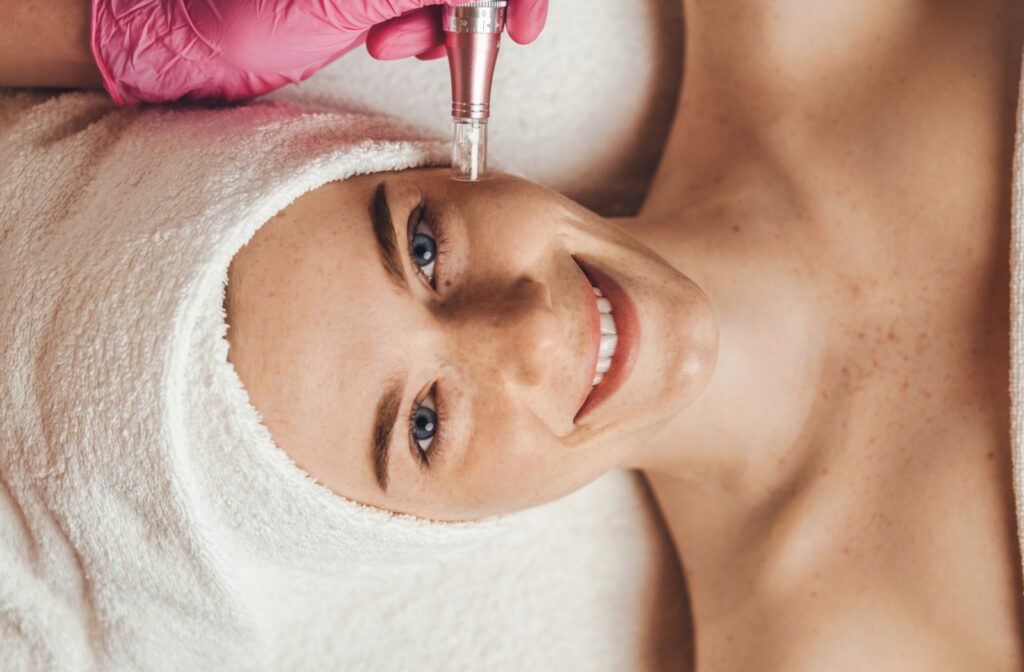 An overhead view of a patient lying down and smiling while an out-of-frame aesthetician performs microdermabrasion on their cheek.