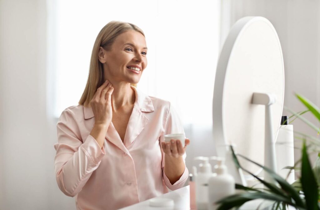 A person rubbing skincare cream on their neck to reduce neck wrinkles while smiling in a mirror.