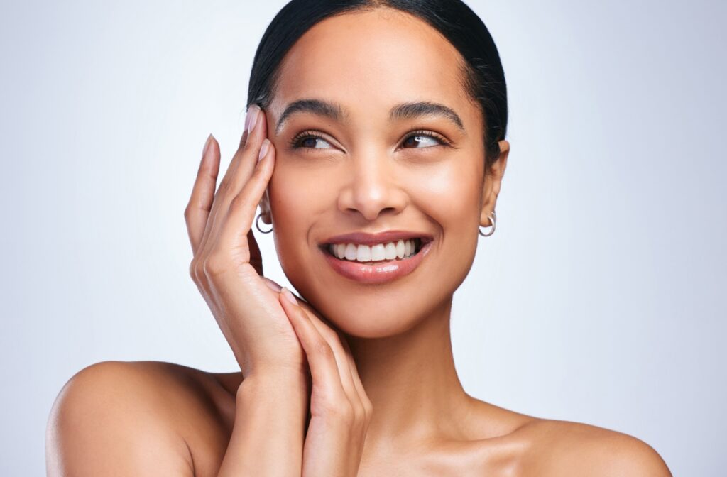 A model looking off to the side and smiling while touching her clear skin